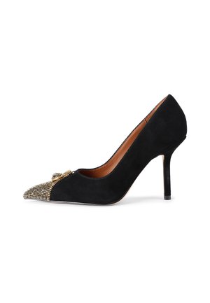Décolleté nera in suede con tacco alto e punta affusolata, caratterizzata da un'applicazione di borchie metalliche sulla punta e un tacco sottile. Fodera interna liscia.