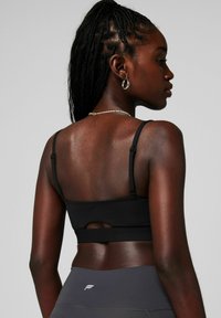 Schwarzer Sport-BH mit dünnen verstellbaren Trägern, einem Schlüsselloch-Ausschnitt auf der Rückseite und einer glatten Textur. Kombiniert mit grauen, hoch taillierten Leggings.