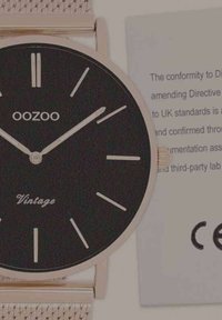 Montre à cadran noir avec bracelet en maille argentée, présentant un design minimaliste, des accents dorés et le texte 'Vintage' sur le cadran. Comprend un label de certification.