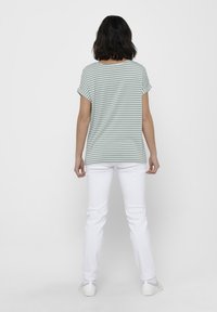 T-shirt rayé vert clair avec des manches courtes retroussées, associé à un pantalon blanc et des baskets. Le tissu semble léger et décontracté.