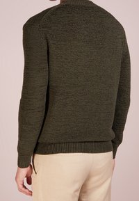 Mörkgrön stickad tröja med rund halsringning och ribbad nederkant. Texturen är slät med ett melerat mönster, lämplig för lager-på-lager.