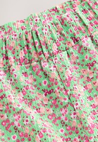 Tissu vert texturé présentant un motif floral dans des tons de rose, rouge et beige ; taille élastiquée avec un détail froncé.