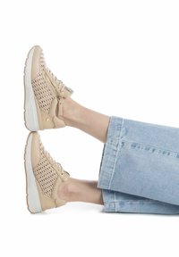 Zapatillas beige con laterales de tela tejida, suela blanca y detalle de cremallera dorada. Combinadas con pantalones de talle alto de mezclilla azul claro.