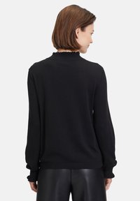 Schwarzer gestrickter Pullover mit einem gerippten Kragen, gewellten Kanten und langen Ärmeln. Weiche Textur, lässiger Schnitt, getragen mit schwarzen Lederhosen.