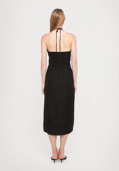 Black halter dress with a smocked bodice, mid-calf length, and a smooth texture. Features thin ties at the neck and a straight skirt.