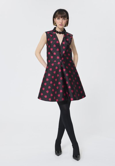 Must have musternikukleid, millel on roosad südame mustrid, V-kaelus ja volangkaelus. Kombineeritud mustade sukkade ja terava nina kontsakingadega.