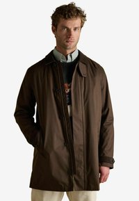 Brązowy, lekki płaszcz o prostym kroju, z zapięciem na guziki z przodu i bocznymi kieszeniami. Posiada klasyczny kołnierz oraz teksturowaną tkaninę.