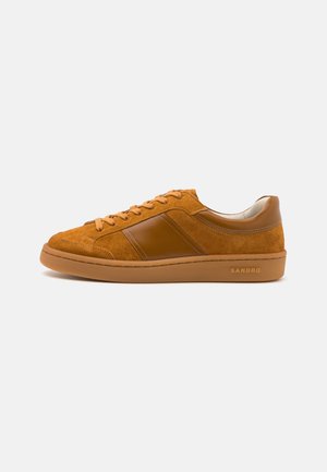 Sneakers din suede maro cu un accent de piele maro neted, vârf rotund și talpă plată din cauciuc. Prezintă șireturi bej și un logo pe lateral.
