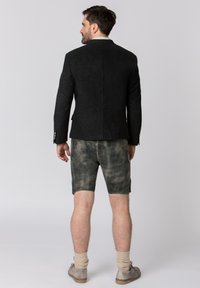 Black wool blazer with a textured finish, paired with knee-length, faded green shorts. Light-colored socks and gray shoes complete the look.