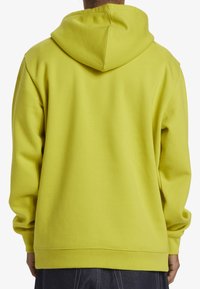 Grön huvtröja med en avslappnad passform, som har en snörning i huvan, ribbade ärmslut och en mjuk textur. Slätt tyg utan synliga mönster.