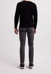 Schwarzer Strickpullover, graue Slim-Fit-Hose und marineblaue Sneakers. Sichtbare Nähte am Pullover und nahtloses Design der Hose.