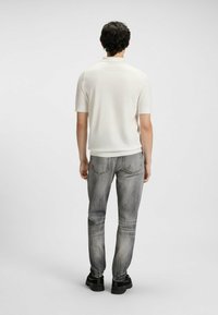 Hvid kortærmet polo-shirt parret med slidte grå jeans og sorte sko, set fra ryggen. Outfittet har et afslappet design.