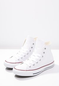 Weiße High-Top-Sneaker aus Canvas mit rundem Zehenbereich, Metallösen und rot-navy gestreiften Akzenten an der Sohle. Klassisches Design.