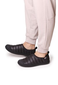 Scarpe nere slip-on con un design imbottito, caratterizzate da una texture trapuntata e una suola in gomma. Indossate con pantaloni chiari.