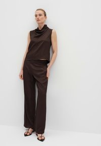 Brown satin sleeveless top with a cowl neck, paired with matching loose-fitting trousers. Model wearing minimalist black sandals.