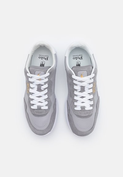 Pantofi sport gri din materiale de velur și piele, având șireturi albe, guler căptușit și un accent cu logo de aur pe lateral.
