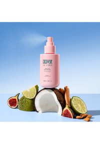 Rosa sprayflaska med pump, märkt "Coco & Eve Like a Virgin," placerad på en kokosnöt, omgiven av lime, fikon, mandlar och kanelstänger.
