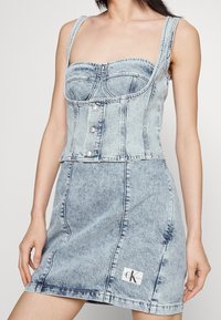 Denim cropped topp och kjol set i ljusblå. Har en åtsittande bodice, stora knappar och CK-logotyp patch på kjolen. Strukturerad tyg.