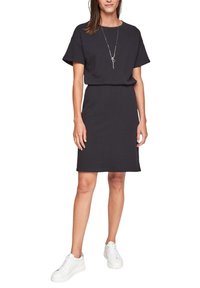 Vestido negro de mezcla de algodón con mangas cortas, escote redondo y cintura ajustada. Combinado con zapatillas blancas para un look informal.