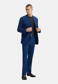 Giacca da abito blu da uomo con pantaloni abbinati, realizzata in tessuto morbido, dotata di chiusura a un pulsante e scarpe nere. Design minimalista.