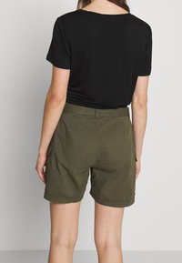 Musta lyhythihainen t-paita yhdistettynä oliivinvihreisiin cargo-shortsien. Shortseissa on sivutaskut ja huolitellut reunat.