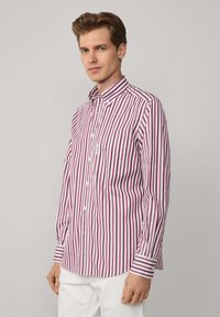 Button-up-Shirt mit vertikalen roten und weißen Streifen, langen Ärmeln, einem spitzen Kragen und einer einzelnen Brusttasche. Der Stoff wirkt glatt und leicht.