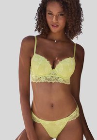 Bledozelený čipkovaný bralet a zodpovedajúce tangá s vykrojenými okrajmi, kvetinovými vzormi a centrálnou dekoráciou na bralete.