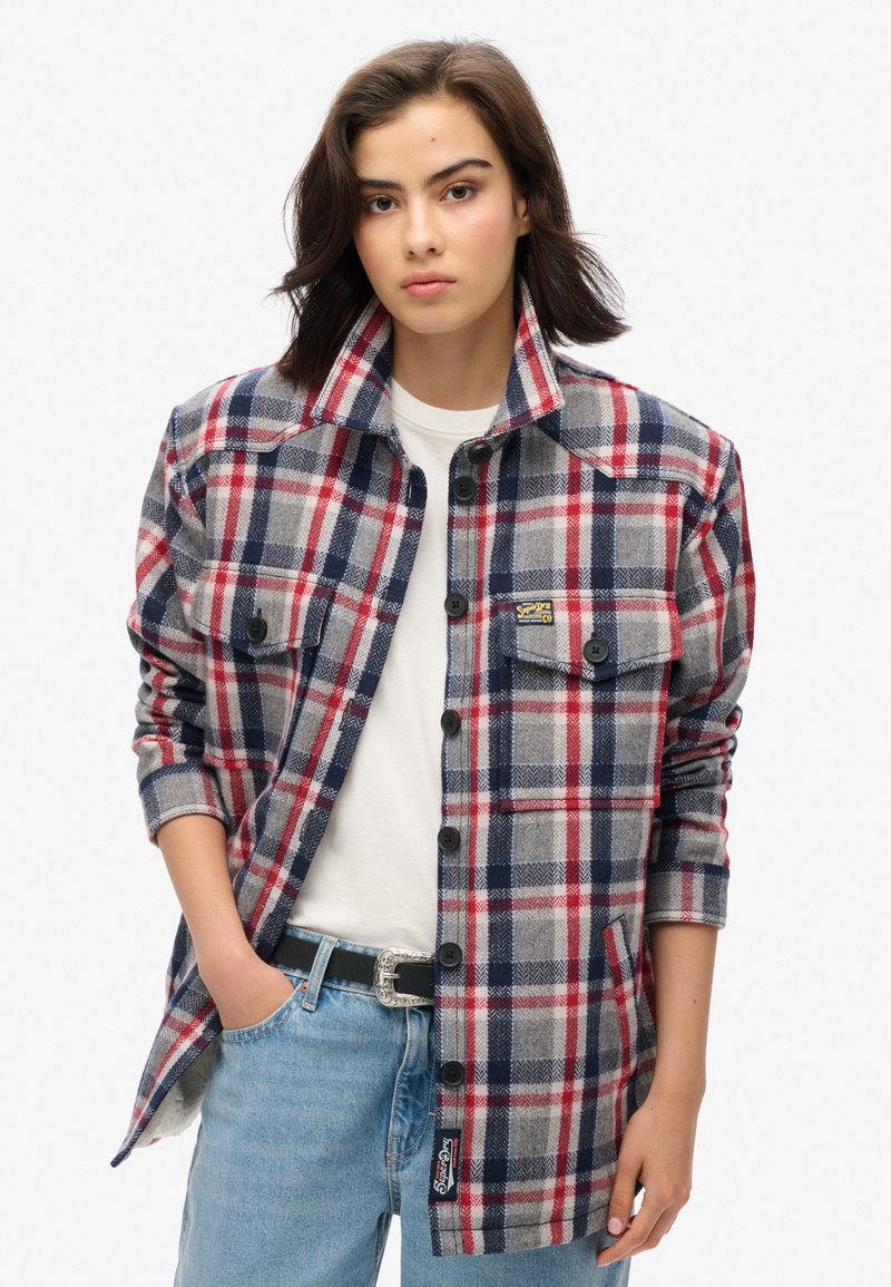 Rutig flannel skjorte i grå, rød og blå med knaplukning foran, to brystlommer og et mærke på siden. Casual pasform og tekstureret stof.
