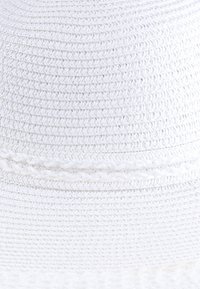 Biały, pleciony kapelusz ze słomy z teksturowanym wykończeniem, zdobiony plecioną opaską wokół korony i szerokim, zaokrąglonym rondem.