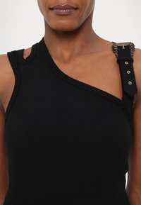Black ribbed tank top with an asymmetrical neckline, featuring a decorative strap with gold accents on one shoulder.