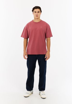 Korte mouwen, ronde hals, rozenkleurig t-shirt van katoen, gecombineerd met donkerblauwe jeans. Witte sneakers maken de outfit compleet.