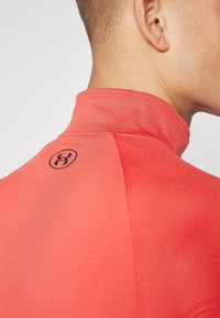 T-shirt de sport rouge avec un col haut, présentant une texture lisse et un accent de logo noir à l'arrière. La vue rapprochée met en évidence les détails du design.