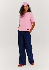 Svetloružový pletený sveter s krátkym rukávom, tmavomodré široké nohavice a červené topánky. Sveter má malú značkovú nálepku na spodku.