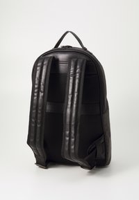 Crna kožna ruksak s mrežastim panelima, podstavljenim trakama i gornjom drškom. Ima glatku teksturu i strukturirani oblik. Zatvaranje na patentni zatvarač.