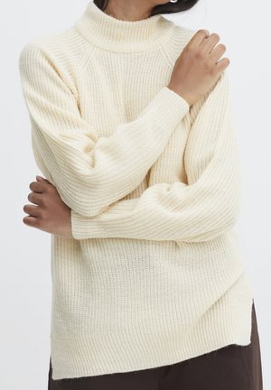 Pull en maille écru à col montant, texture côtelée et manches longues ; possède une coupe décontractée et des fentes latérales à l'ourlet.
