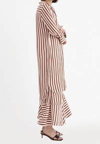 Randig klänning i röd och beige med en lång silhuett, volangärmskant och sidoklyftor, tillverkad av ett lätt material.