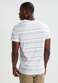 White short-sleeved T-shirt with geometric blue patterns, round neckline, and a slim fit. Smooth cotton fabric and subtle texture.