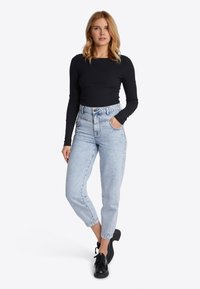Zwarte ribbelige top met lange mouwen, gecombineerd met lichtblauwe denim jeans met hoge taille. De jeans hebben een lichte taper en zijn cropped op enkelhoogte. Zwarte veterschoenen.