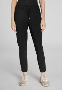 Pantalones jogger negros con un diseño ajustado, que cuentan con una cintura con cordón y bolsillos laterales con cremallera, fabricados en una tela suave y elástica.