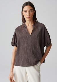 Blusa a righe marrone e crema con una vestibilità rilassata, maniche corte e colletto a scollatura. Tessuto morbido con una texture liscia.