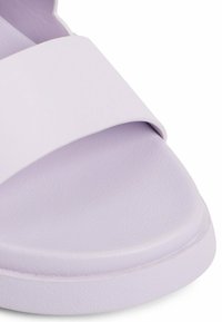 Lila slip-on sandal med en bred, slät rem och en texturerad fotbädd. Rundad sula för komfort och stabilitet.