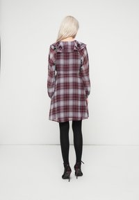 Πλαϊδ φόρεμα σε σκούρο μπορντό και γκρι αποχρώσεις, με ραμμένο κολάρο και μακριά μανίκια. Φοριέται με μαύρες καλσόν και παπούτσια με τακούνι.