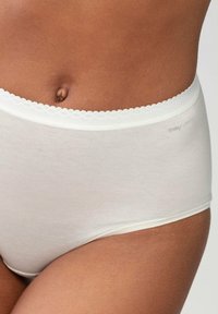 Frau trägt hochgeschnittene, weiße Baumwollunterwäsche mit einem gewellten elastischen Bund und "mey LIGHTS"-Markierung auf der rechten Seite.