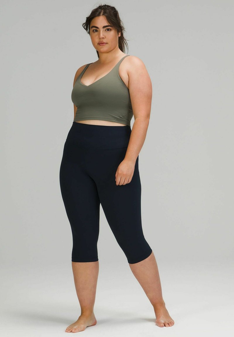 Bralette de sport vert olive avec un décolleté en V associé à un legging capri marine taille haute, tous deux en matière lisse et extensible.