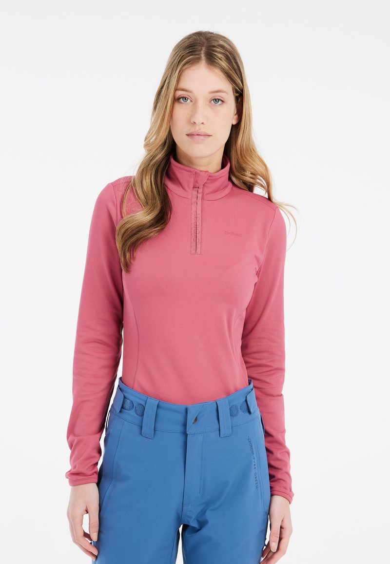 Pullover rosa a maniche lunghe con colletto a zip a un quarto, abbinato a pantaloni blu con cintura con bottone e tasche slanciate.