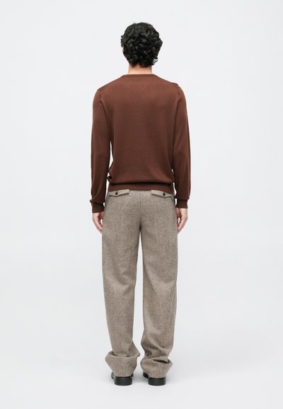 Pullover castanho de malha com mangas longas, combinado com umas calças texturizadas de tom cinza claro. As calças apresentam bolsos laterais e detalhes em botão.