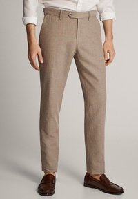 Beige, op maat gemaakte broek van lichtgewicht stof, voorzien van een platte voorkant, riemlussen en een enkele knoopsluiting.