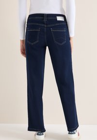 Jeans rectos de color azul marino con dos bolsillos traseros, costuras sutiles y una etiqueta de la marca en la cintura, combinados con zapatillas blancas.