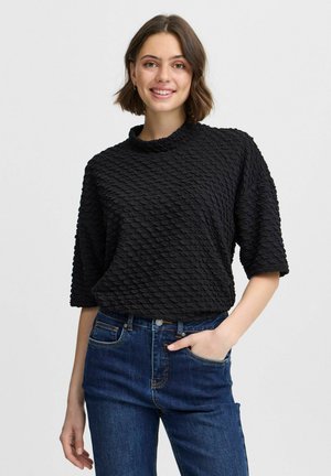 Schwarzes, strukturiertes Oberteil mit hohem Kragen, kurzen Ärmeln und einem gemusterten Oberfläche. Kombiniert mit dunkelblauen Jeans.