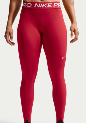Άτομο που φοράει στενά κόκκινα κολάν Nike Pro με λευκό λογότυπο Nike στο αριστερό μηρό και σήμανση Nike Pro στη μέση.